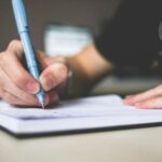 Close-up of hand writing in notebook using a blue pen, focus on creativity.